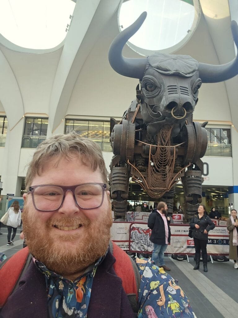 Stephen stood smiling infront of the Birmingham Bull at Birmingham New Street train station