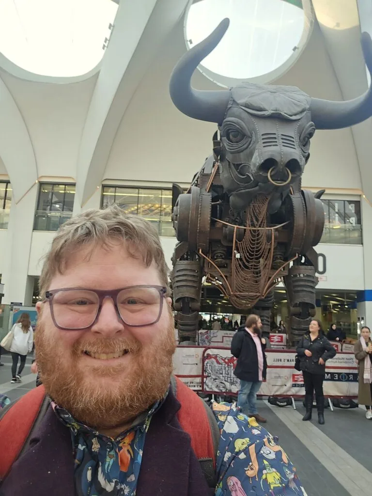 Stephen stood smiling infront of the Birmingham Bull at Birmingham New Street train station